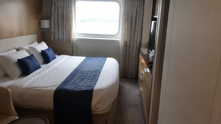 Cruise cabin with a double bed, blue cushions, and window