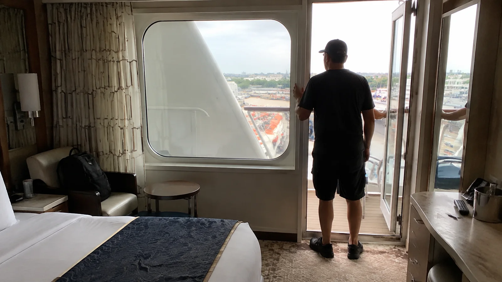 Man standing in a cruise cabin balcony doorway beside an obstructed window