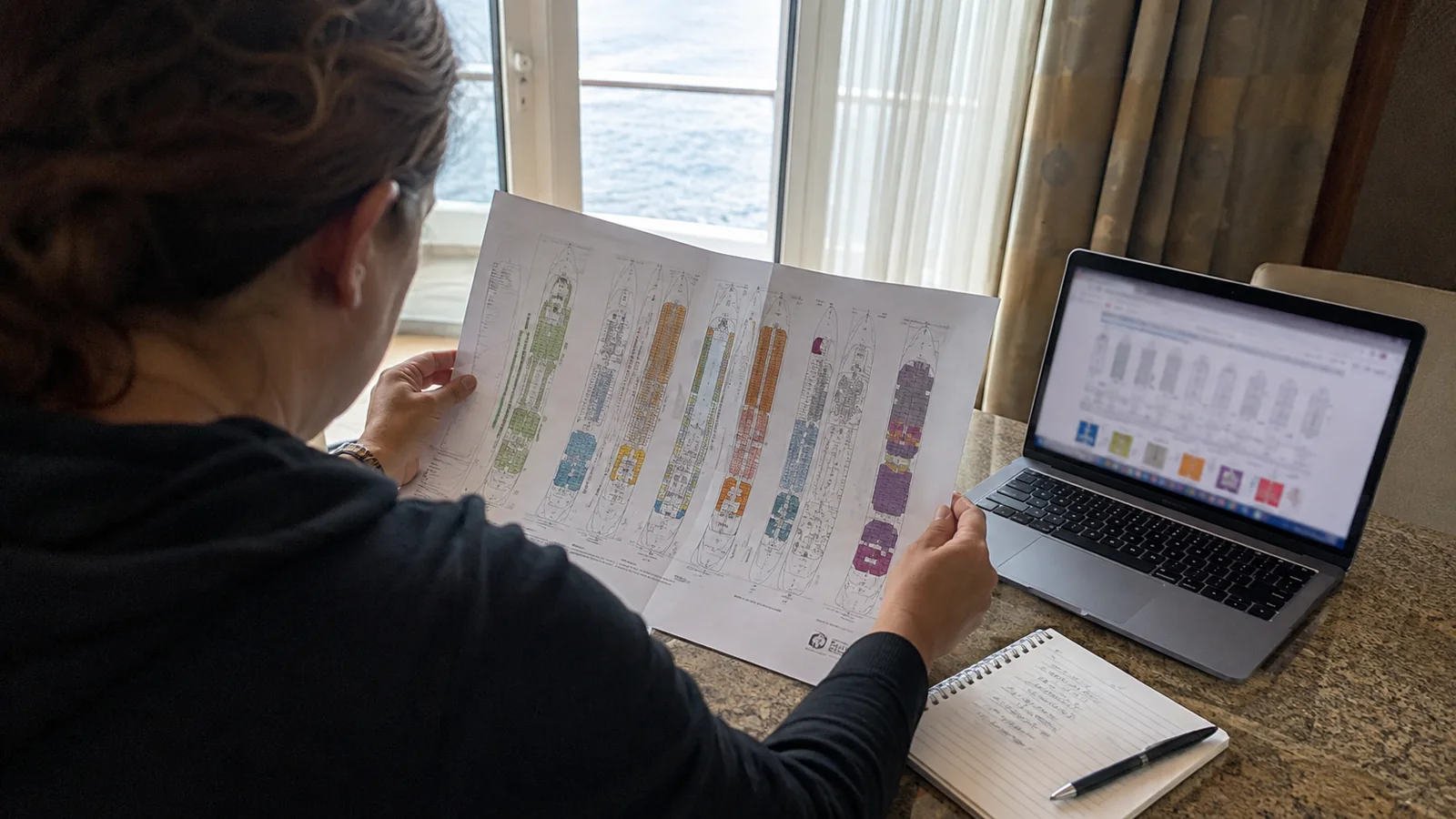 Woman holding a printed cruise ship deck plan beside a laptop