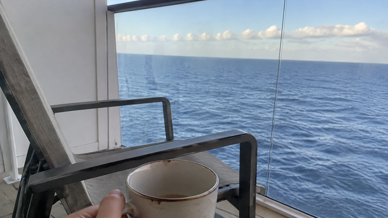 Coffee cup beside a balcony chair overlooking open water.