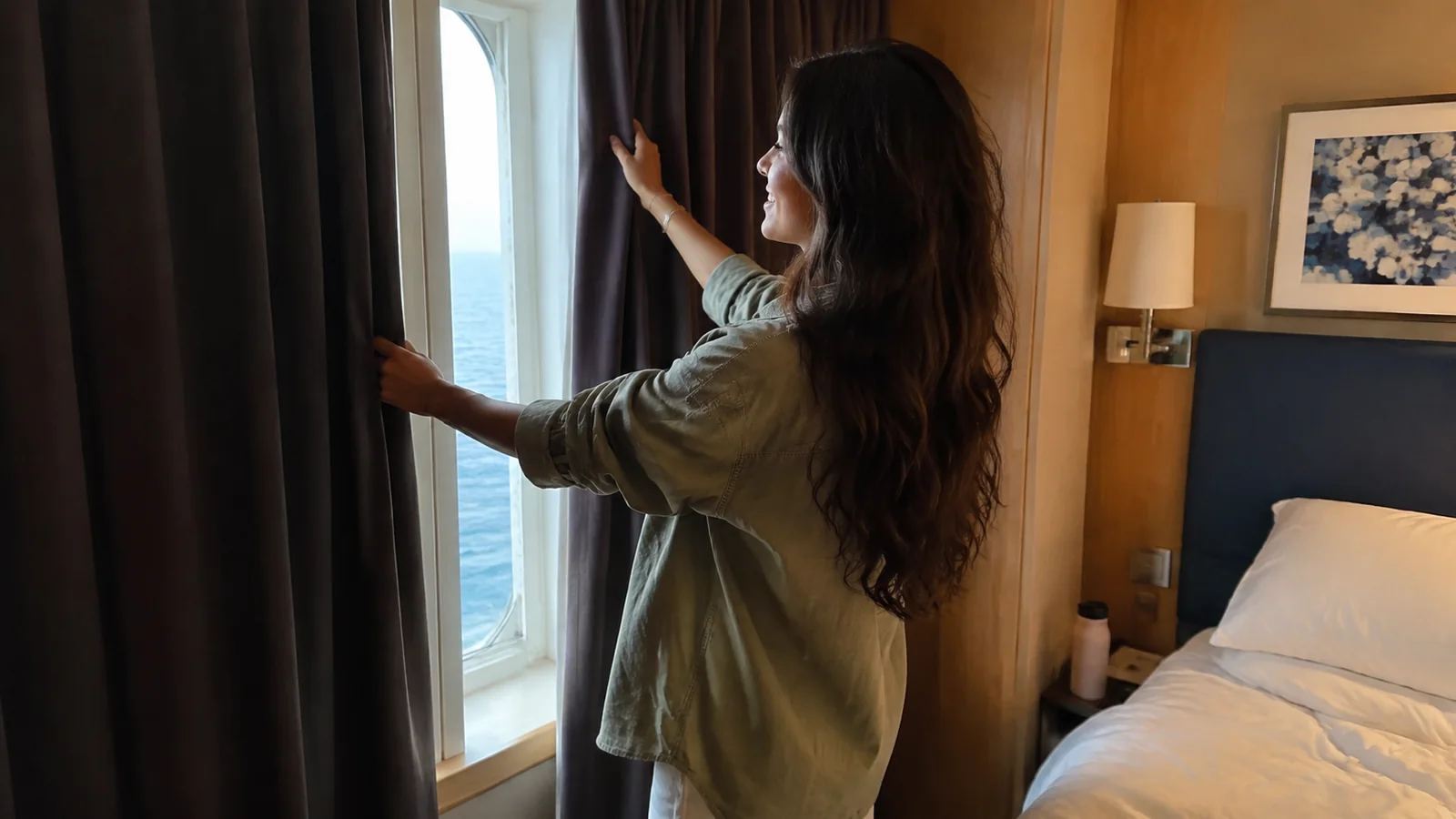 Woman opens curtains beside a cabin balcony door.