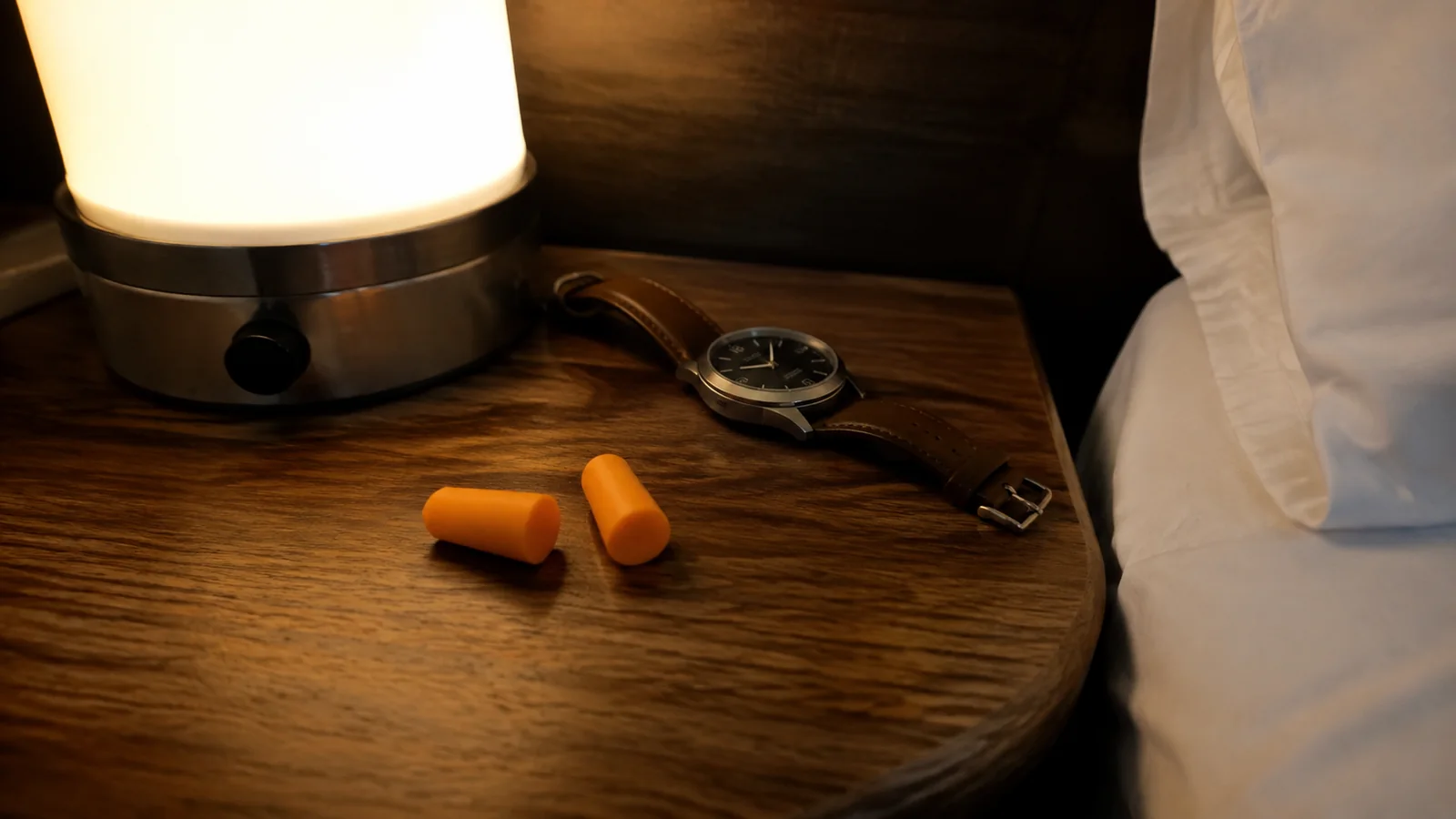 Orange earplugs and a wristwatch rest beside a bedside lamp.