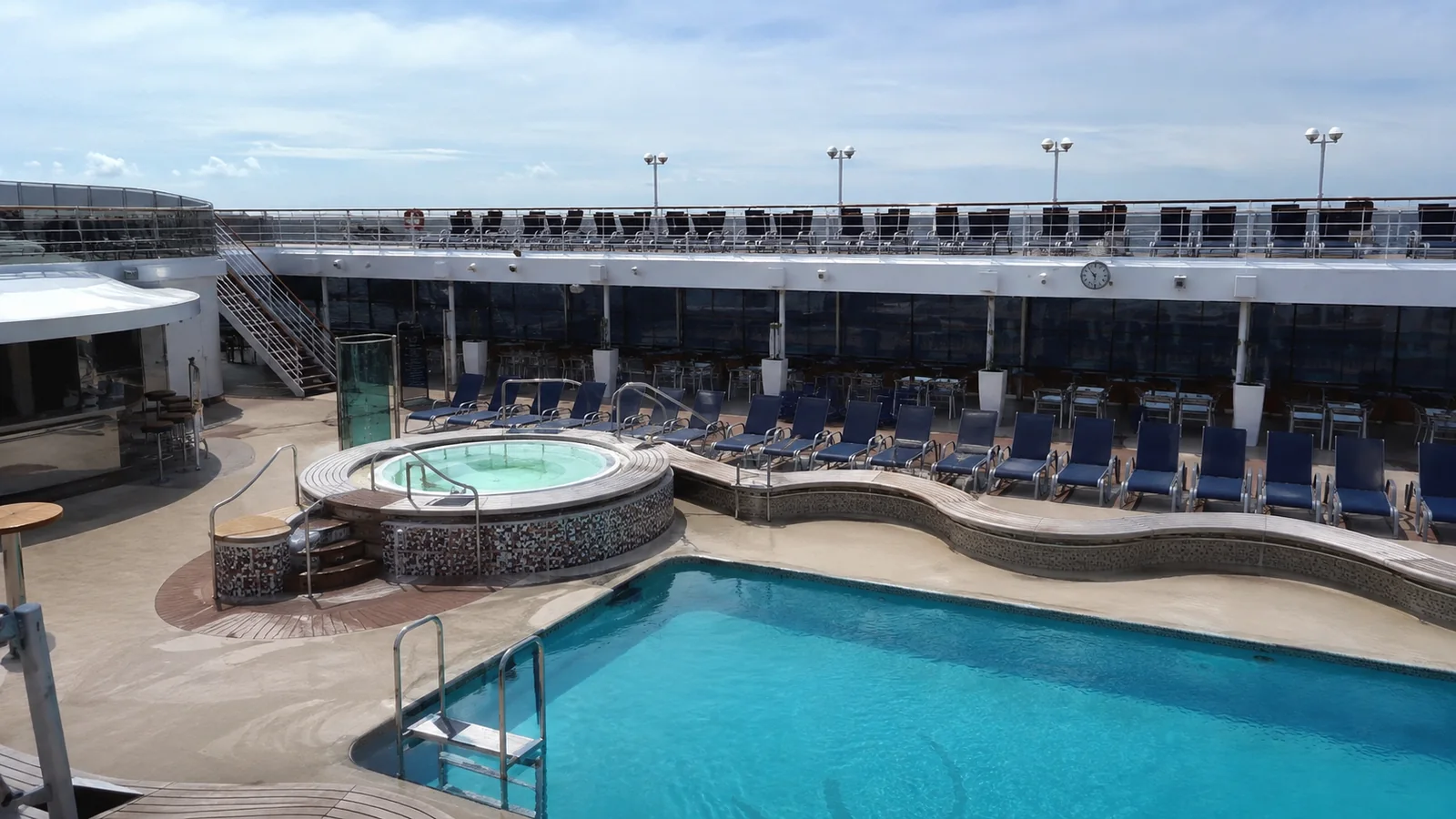 Swimming pool and hot tub surrounded by lounge chairs on a ship.