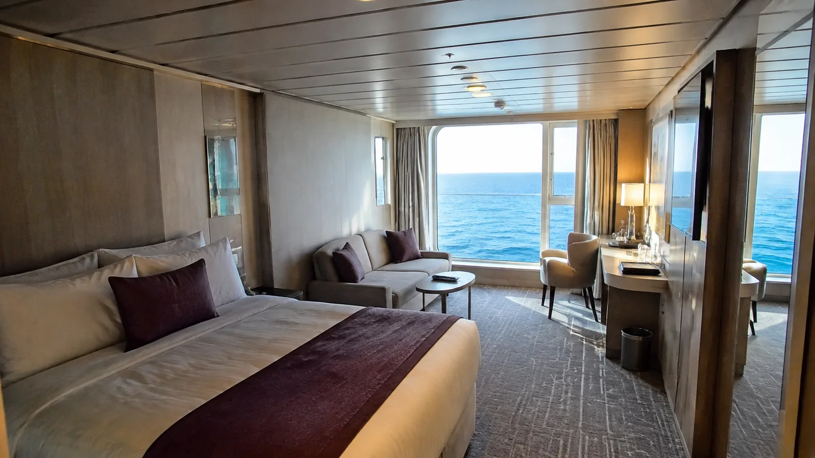 Cruise cabin with a double bed, sofa and a large ocean-facing window.