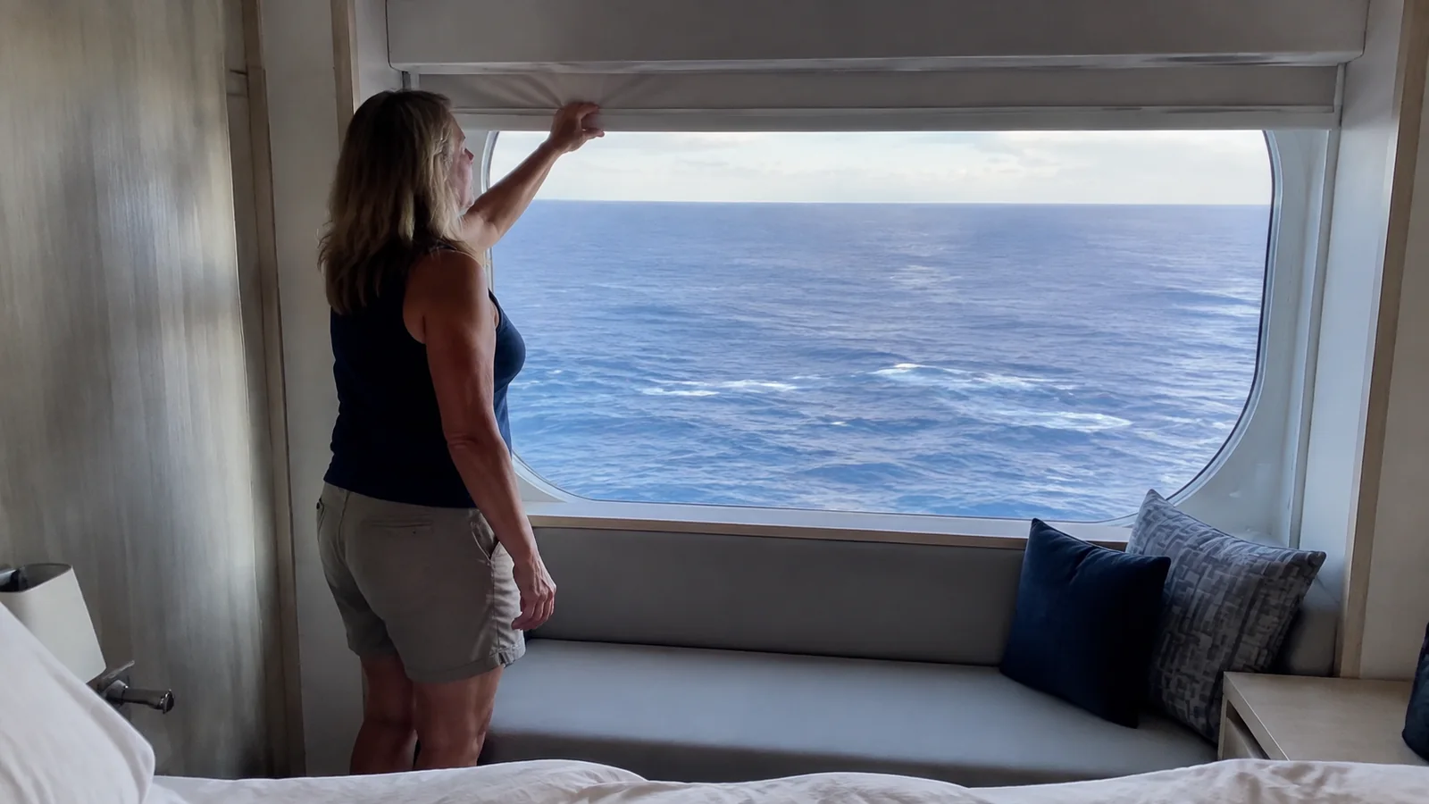 Passenger raising a blind above a large cabin window.