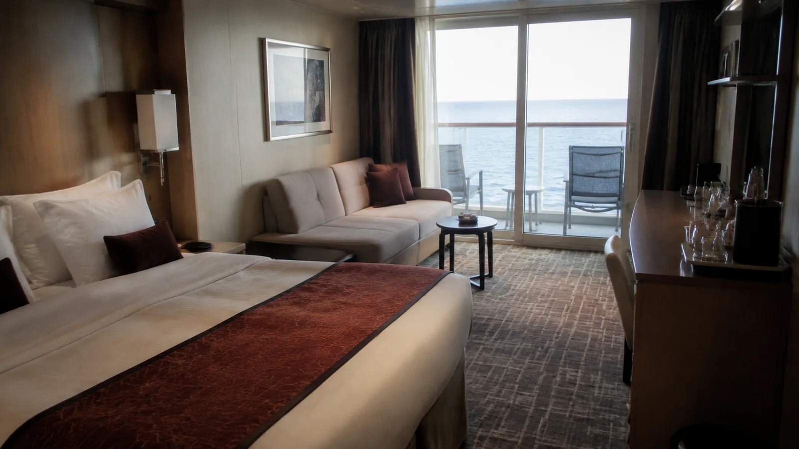 Ship cabin with a red bed runner, sofa, and balcony doors.