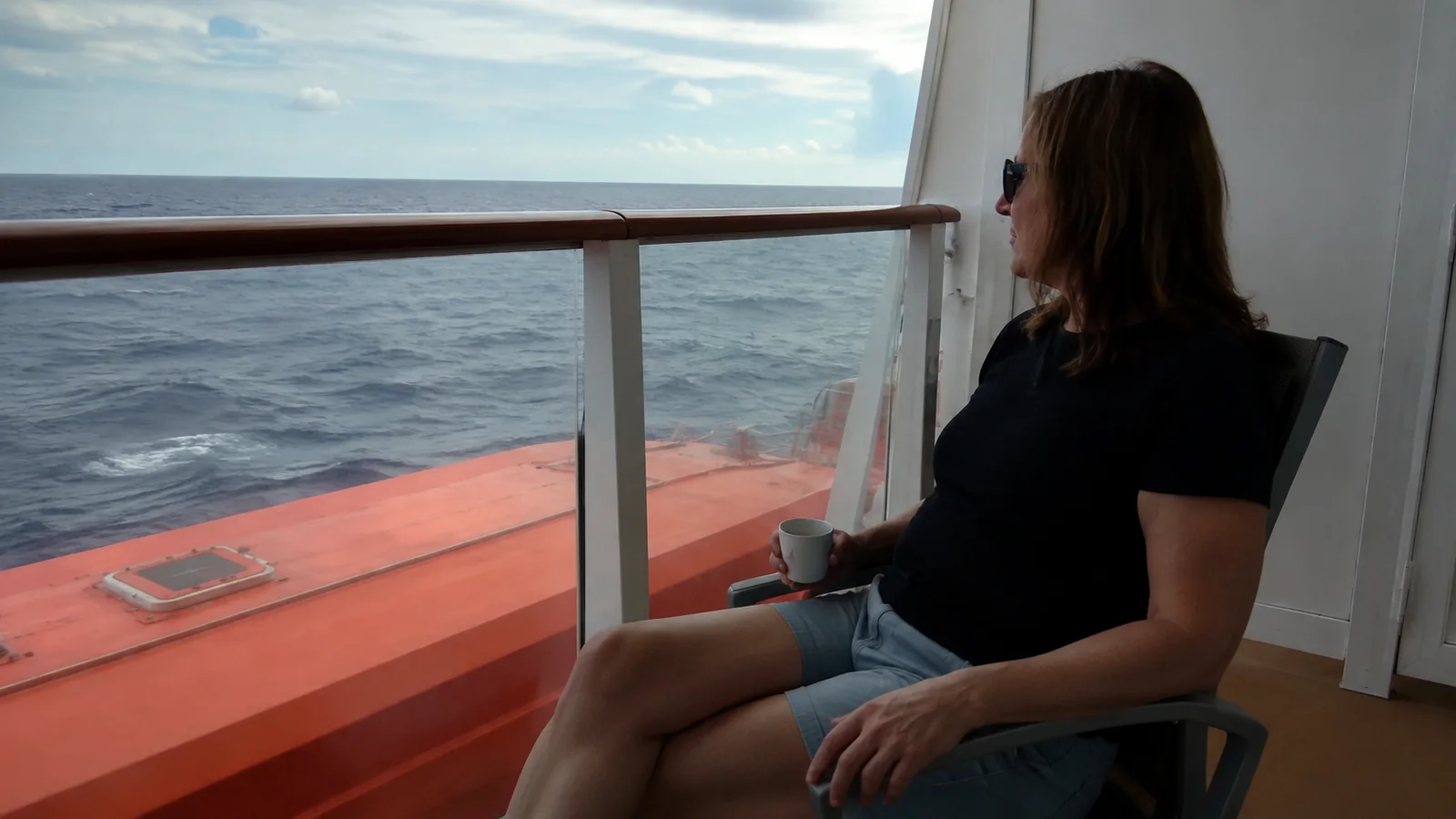 Woman seated on a balcony above an orange lifeboat.
