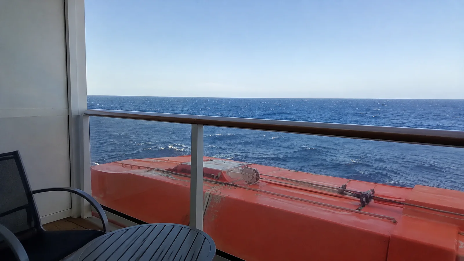 Orange lifeboat partially obstructing an ocean view from a ship balcony.