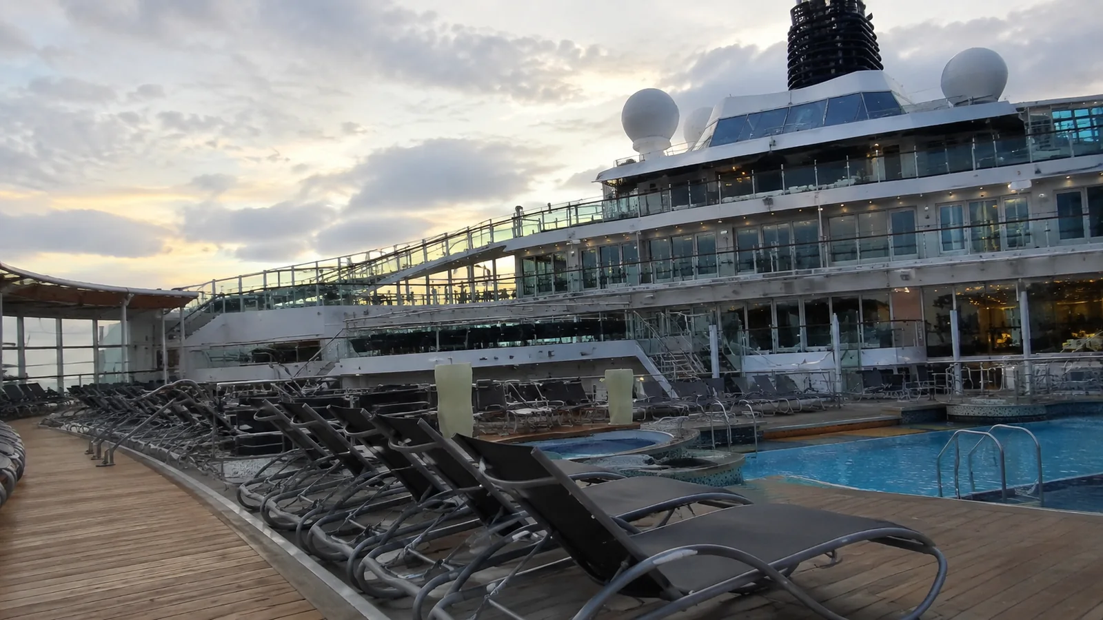 Empty ship pool deck surrounded by loungers and upper balconies.