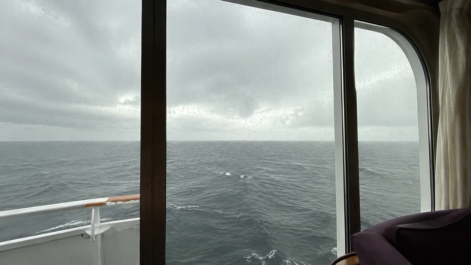 Large ship windows frame gray skies and the open ocean.