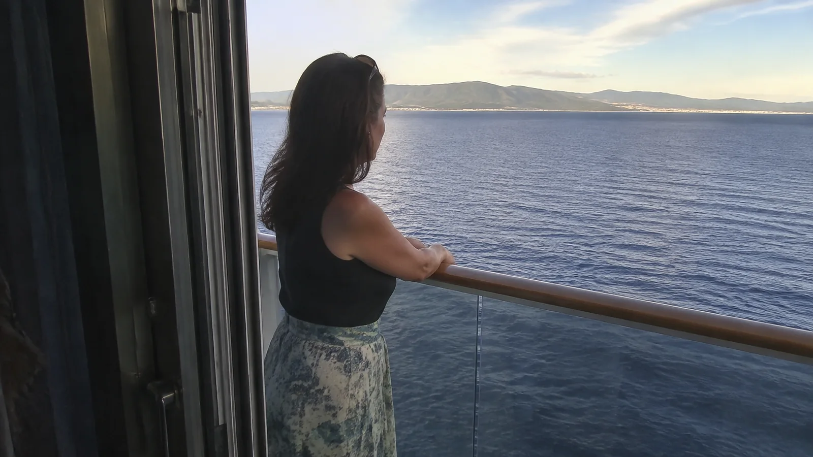 Woman rests her arms on a balcony railing overlooking the sea.