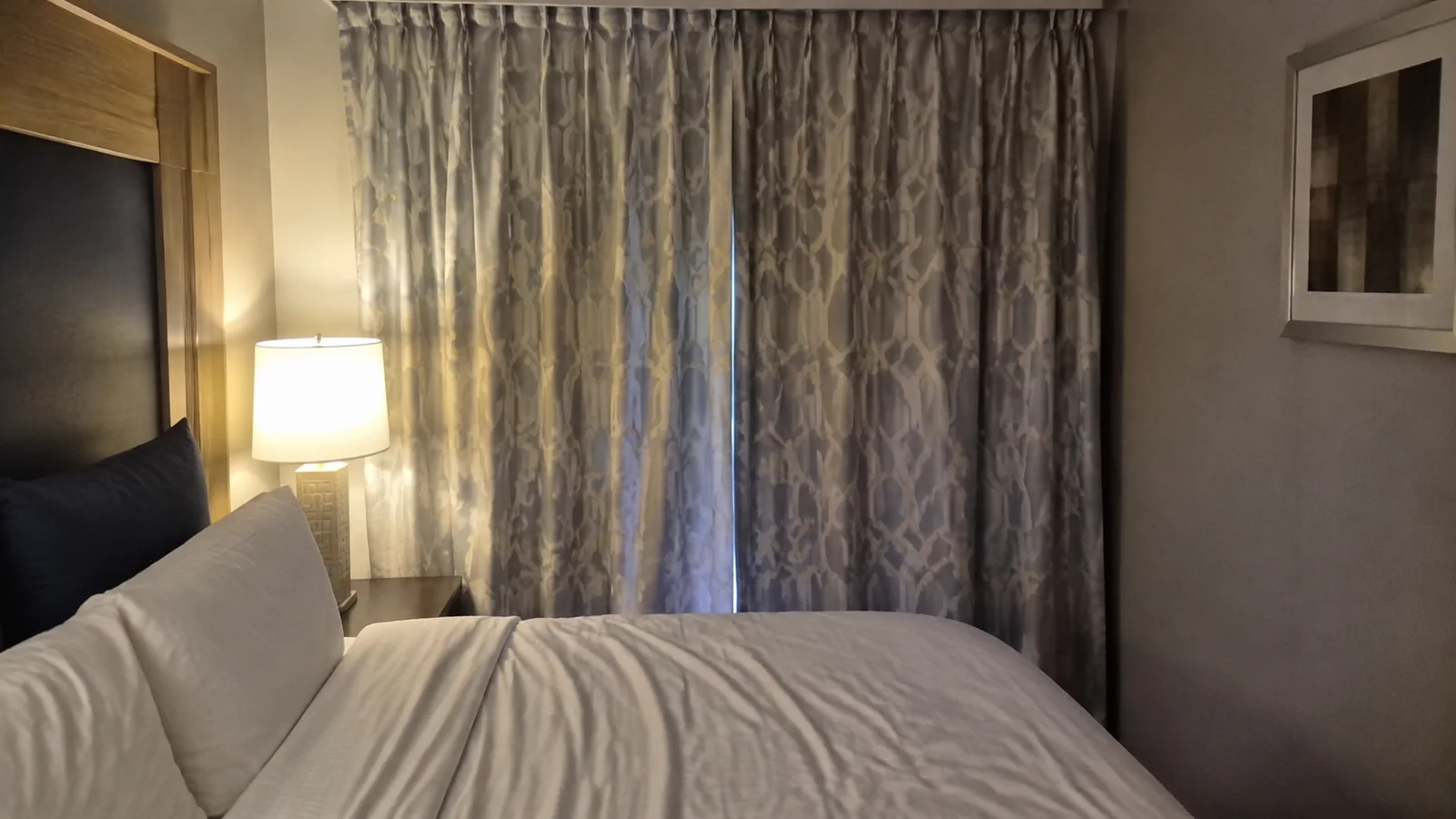 Closed patterned curtains hang beside a stateroom bed and lamp.