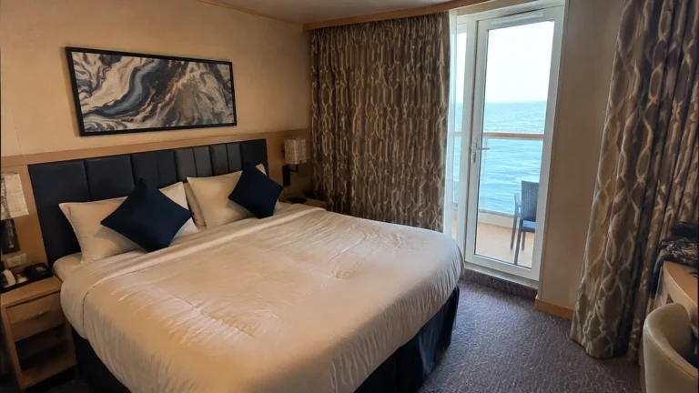 Double bed with blue cushions beside the balcony door in a cruise cabin.