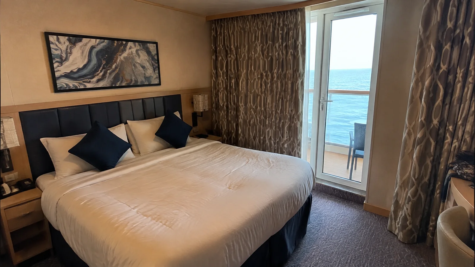 Double bed with blue cushions beside the balcony door in a cruise cabin.