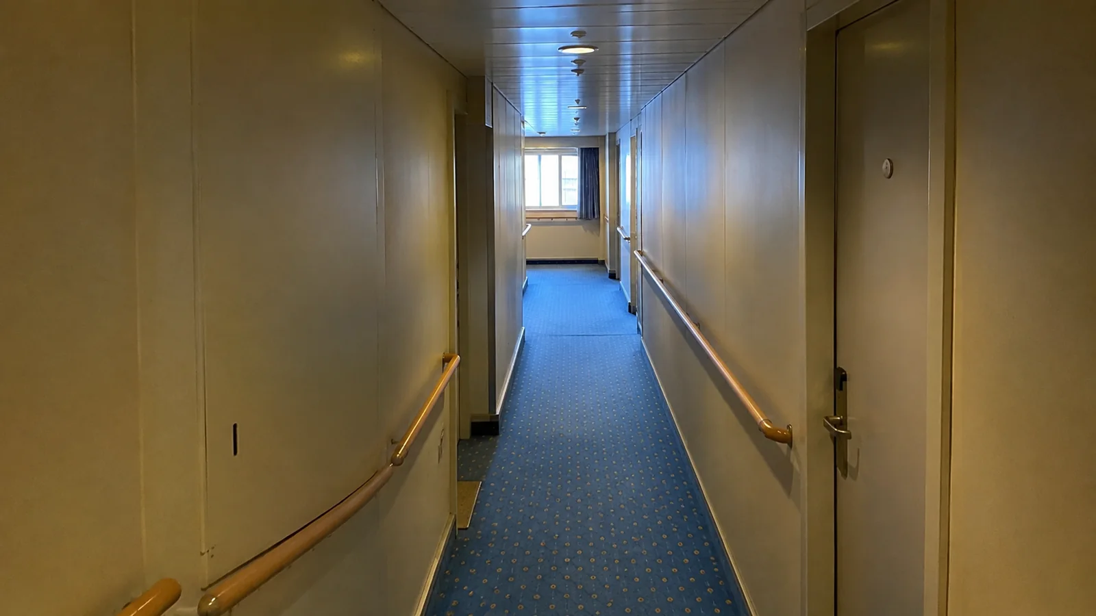 Quiet blue-carpeted corridor with handrails and cabin doors.