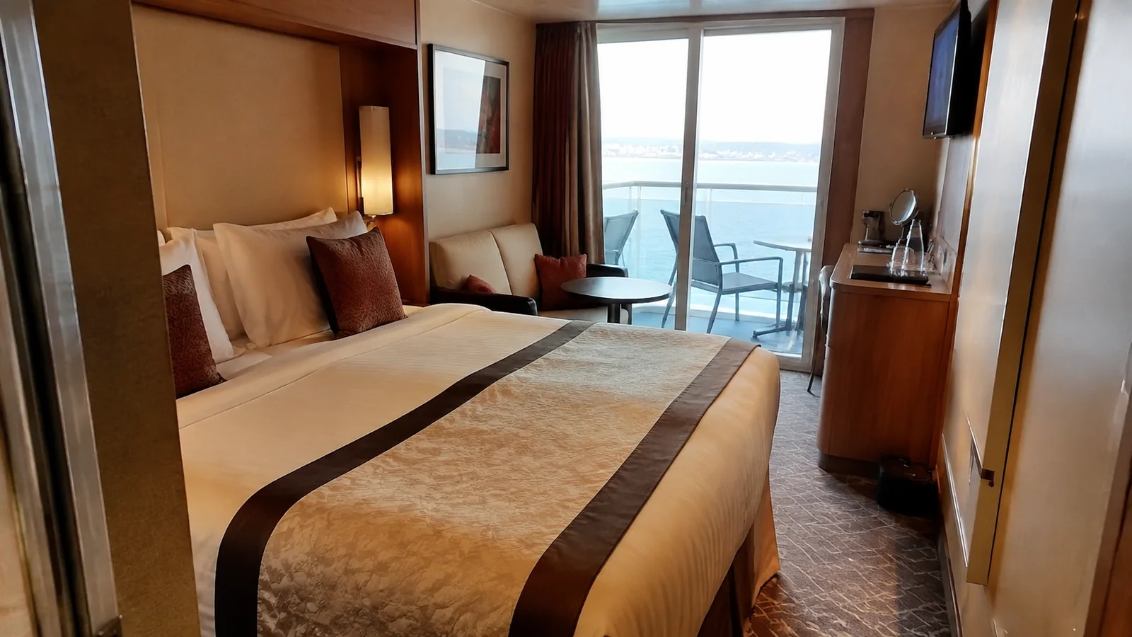 Cruise cabin with a double bed, sofa and balcony overlooking the ocean.