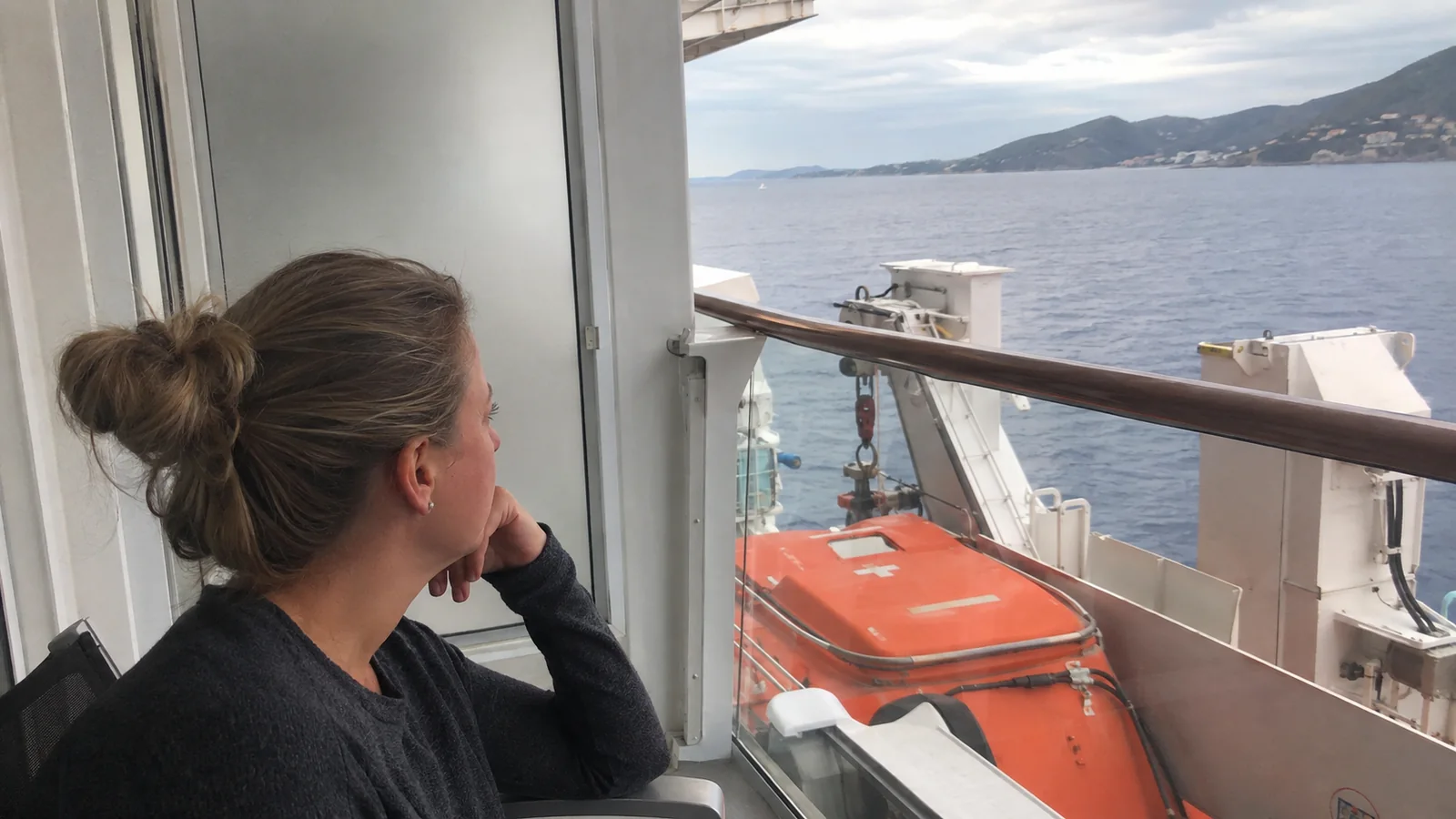 Passenger seated beside a balcony railing above an orange lifeboat.