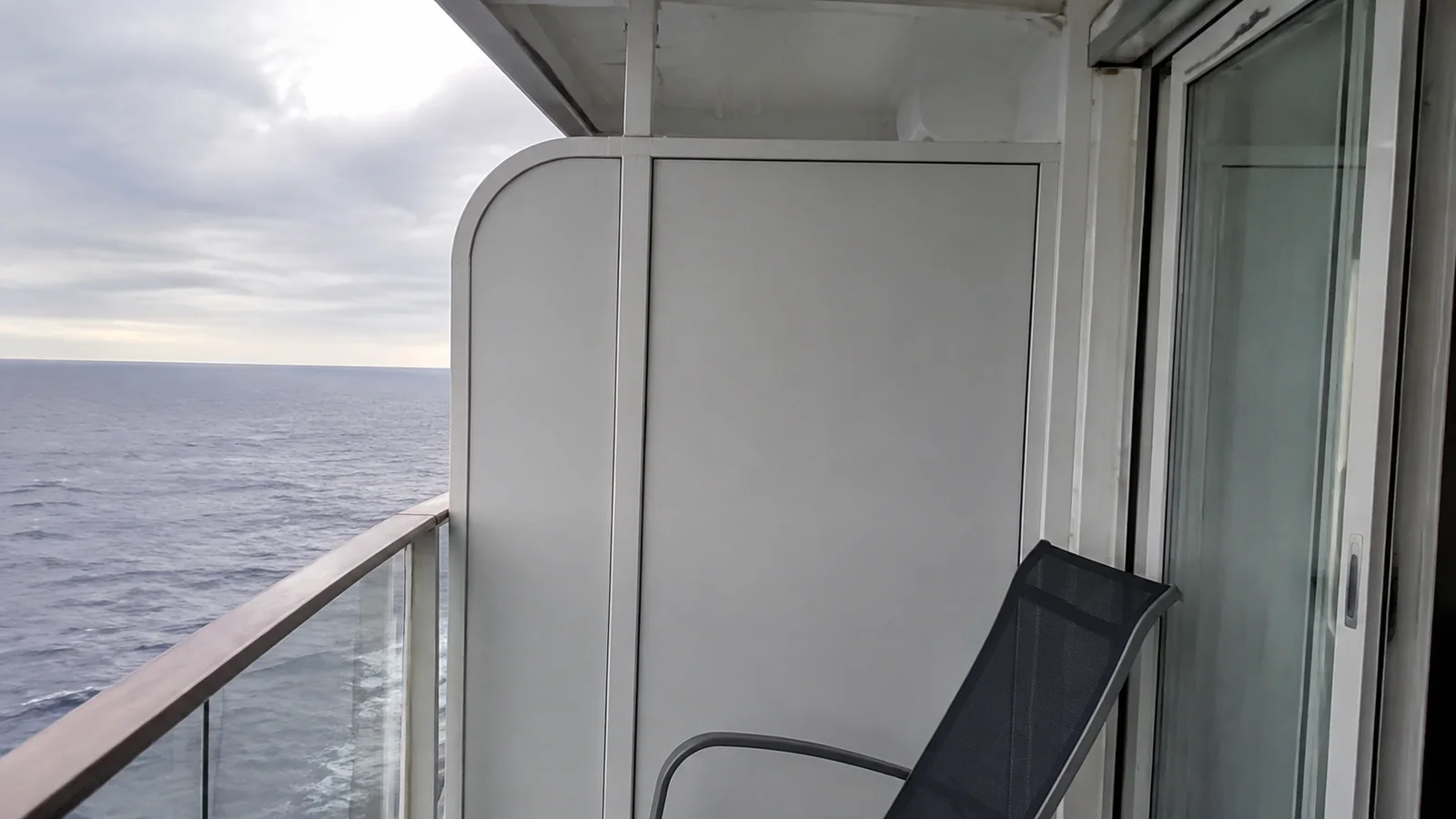 Narrow balcony with a chair beside a tall privacy partition.