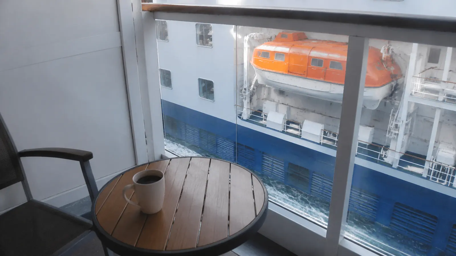 Cruise balcony table and chair with a lifeboat and neighboring ship visible outside