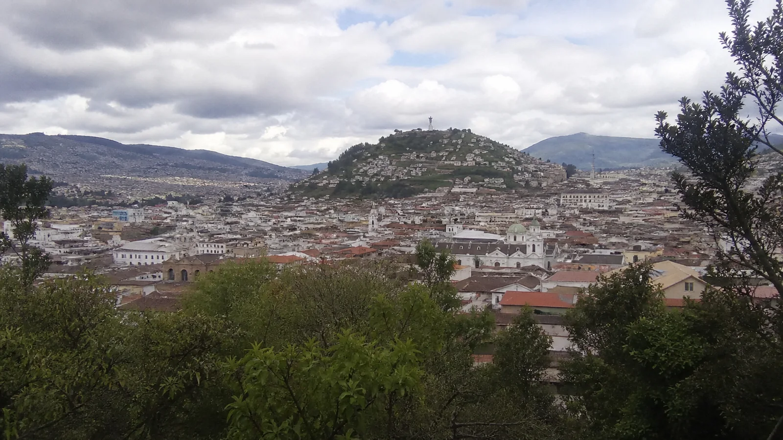 Wide view across a densely built city surrounded by green hills.