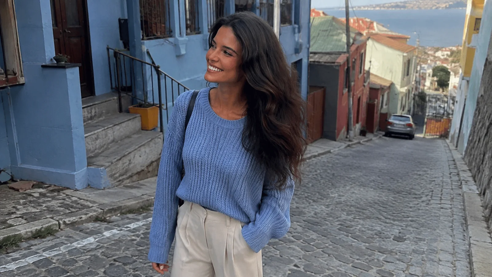 Woman walking down a steep cobblestone street between colorful buildings.