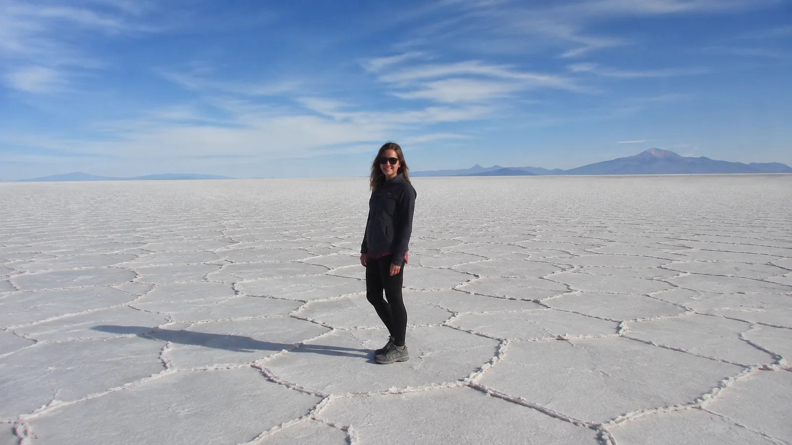 Woman standing on a vast white salt flat beneath distant mountains.
