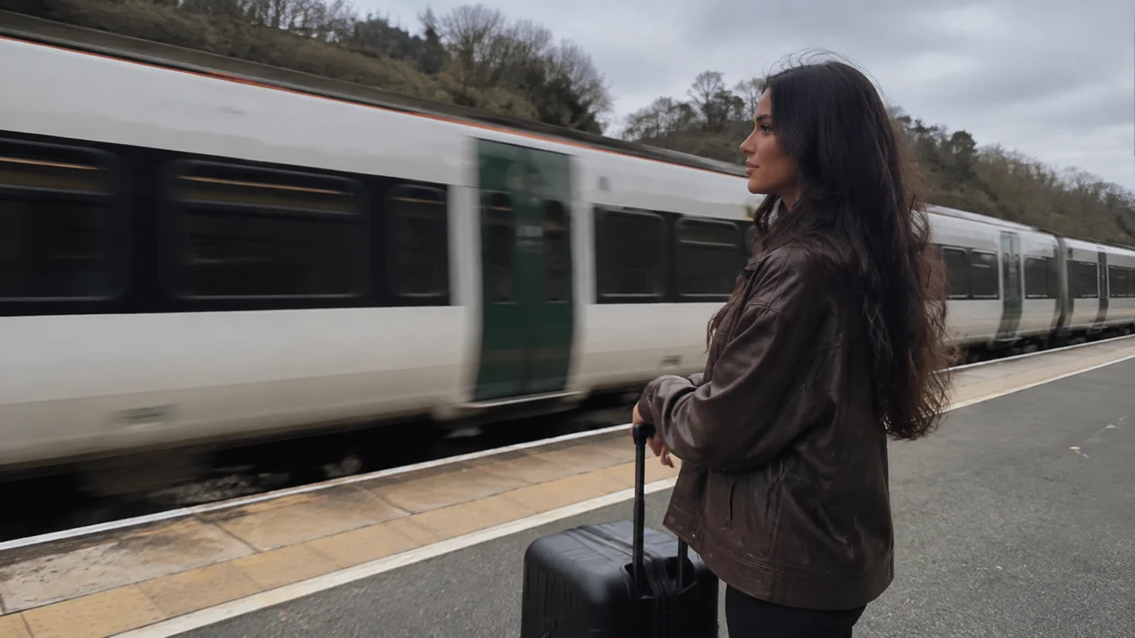 Traveler with a rolling suitcase waiting beside a passenger train.