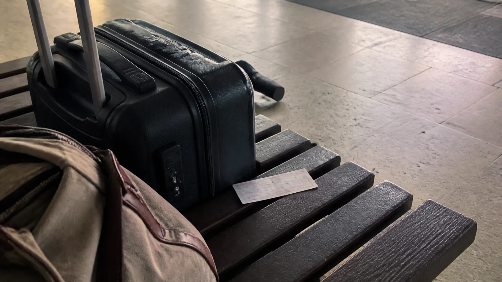 Suitcase and travel bag on a station bench with a paper ticket.
