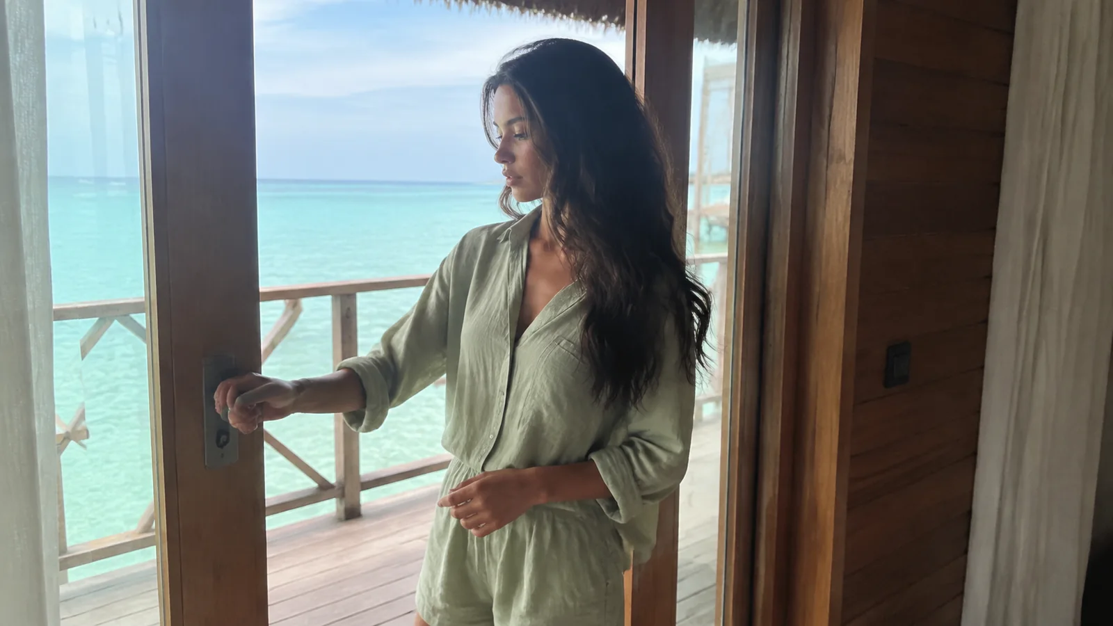 Woman opening glass doors onto an ocean-facing villa deck.