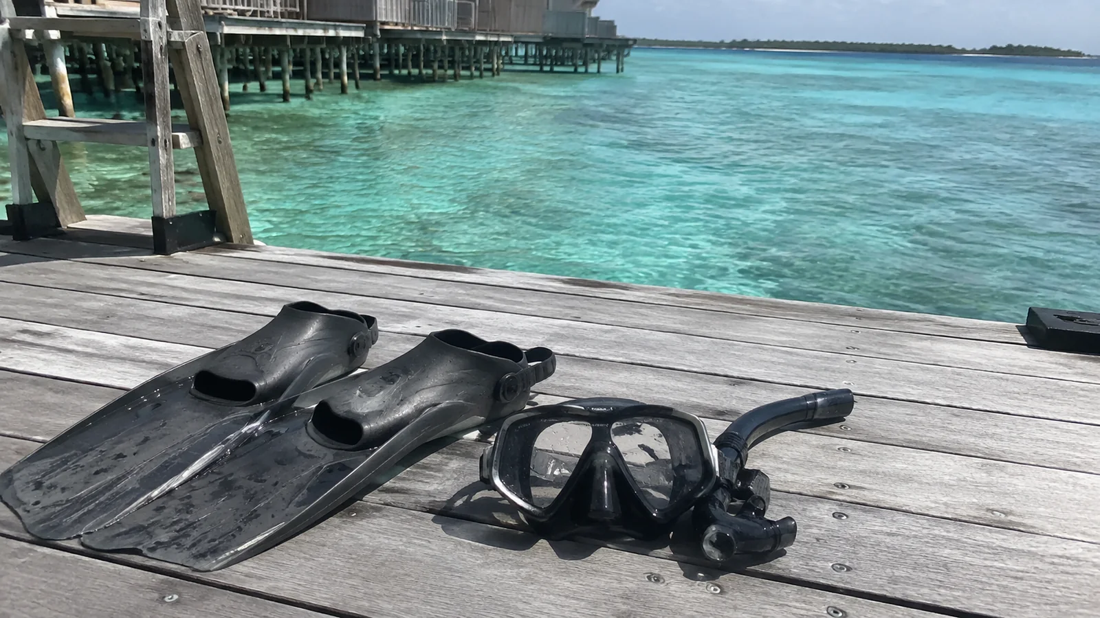 Snorkeling fins, mask and snorkel on a wooden deck beside clear water.