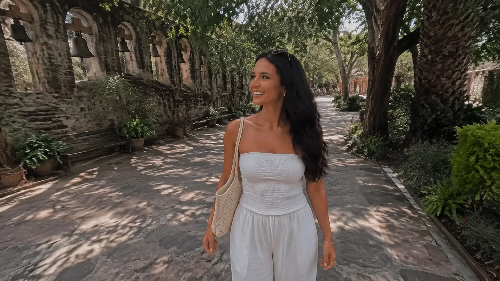 Woman in a white dress walking along a shaded stone-lined path.