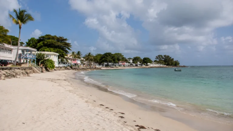 Pale sandy beach with calm water and small waterfront buildings.