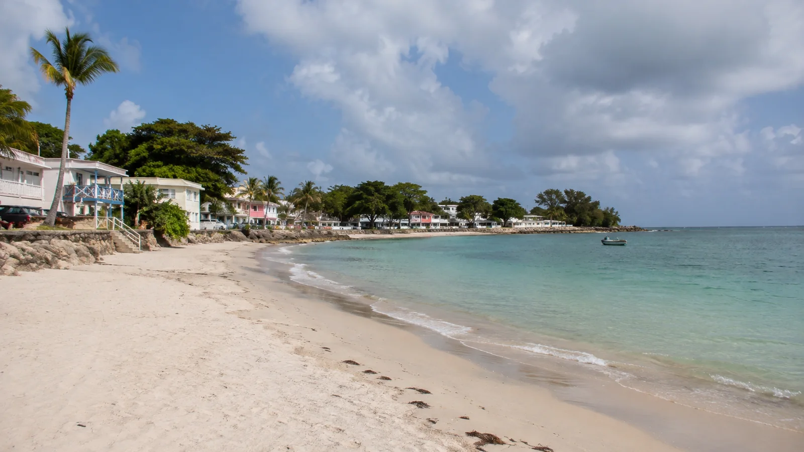Pale sandy beach with calm water and small waterfront buildings.
