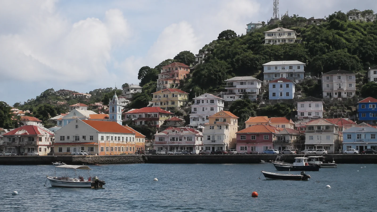 Hillside town with colorful houses overlooking a harbor dotted with small boats.