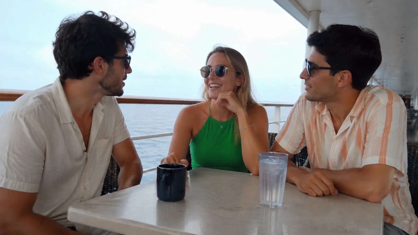 Three friends chatting around a table on an ocean-facing deck.