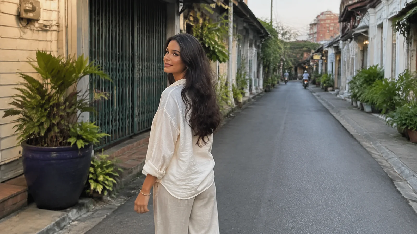 Woman walking a quiet narrow street lined with plants and old buildings.