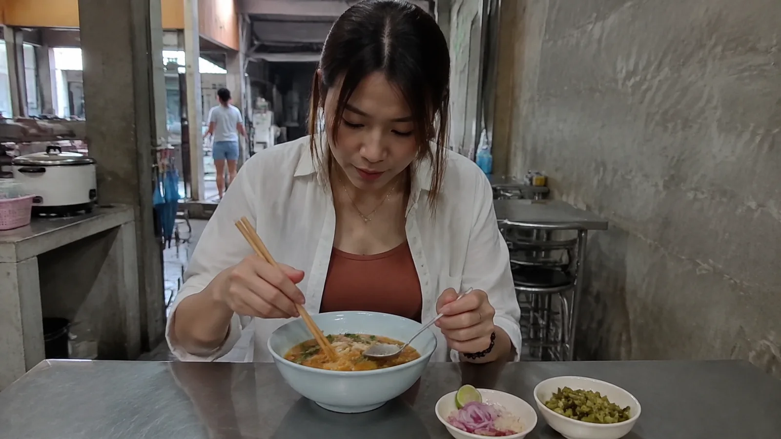 Woman eating a bowl of noodles at a small restaurant.