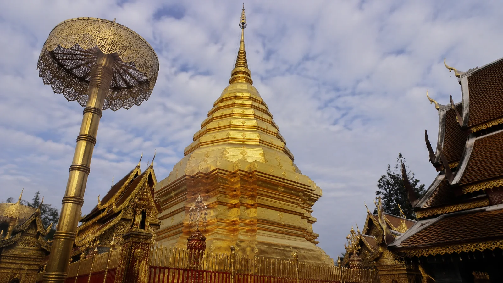 Golden stupa and decorative parasol beside ornate temple roofs.