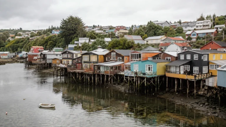 Colorful wooden stilt houses reflected in calm waterfront water.