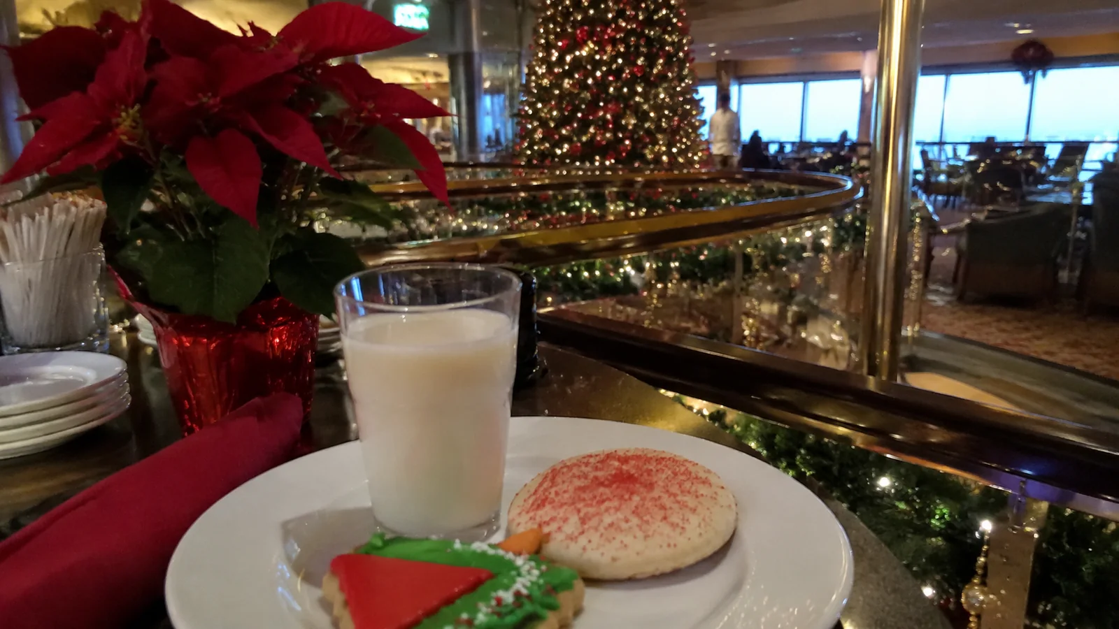 Plate of Christmas cookies and a glass of milk with a decorated tree in the background