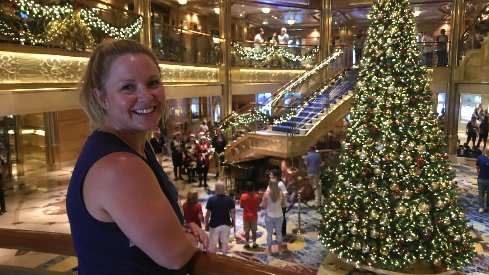 Woman standing in a cruise ship atrium beside a large decorated Christmas tree