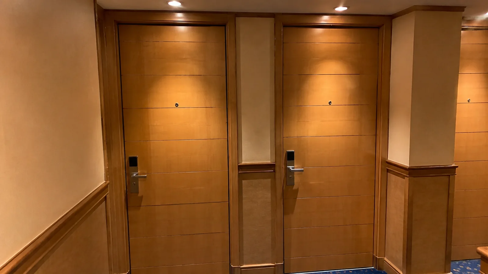 Two adjacent wooden stateroom doors face a warmly lit corridor.