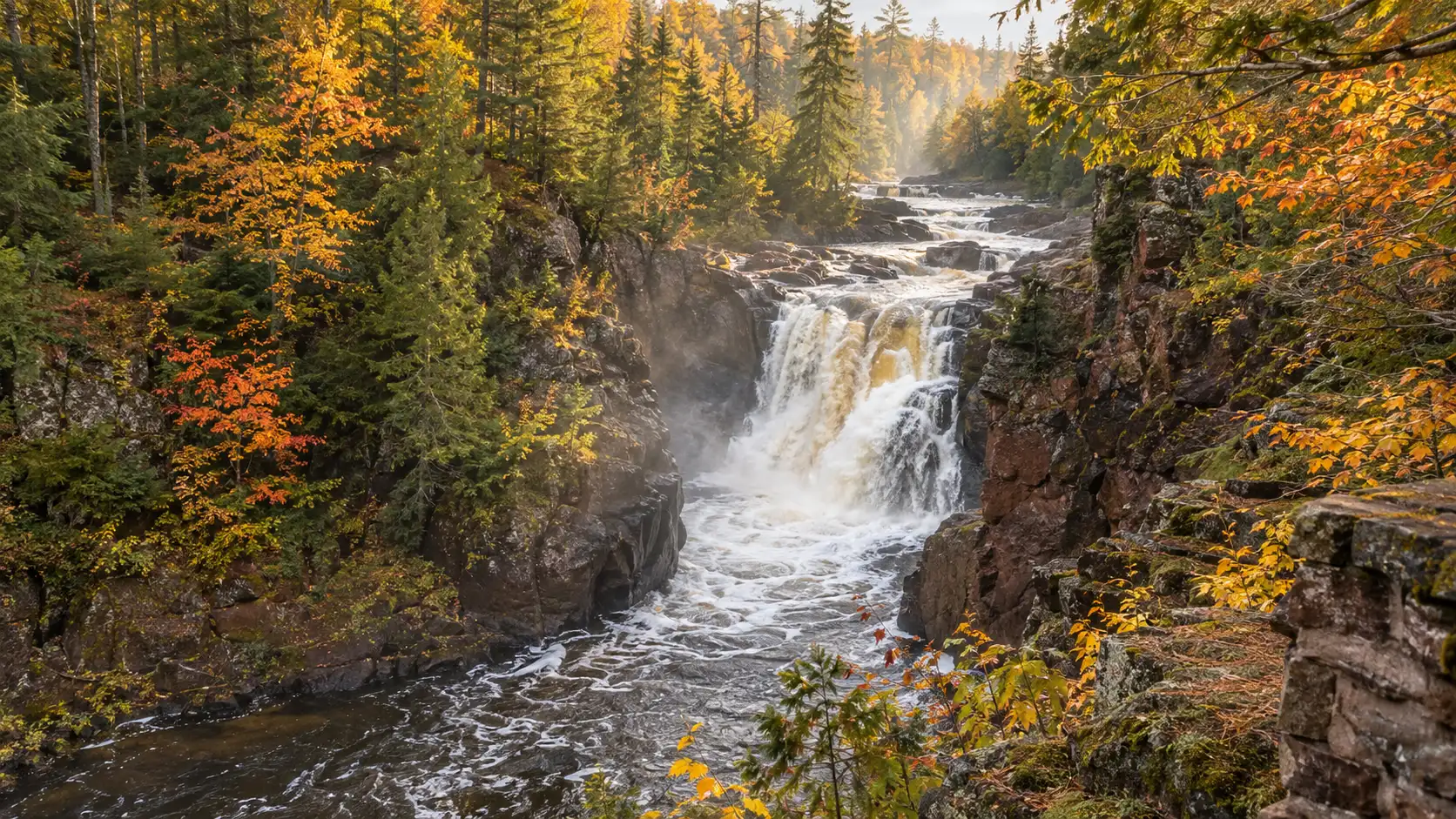 Copper Falls flowing through a red-brown gorge framed by golden autumn forest in northern Wisconsin.