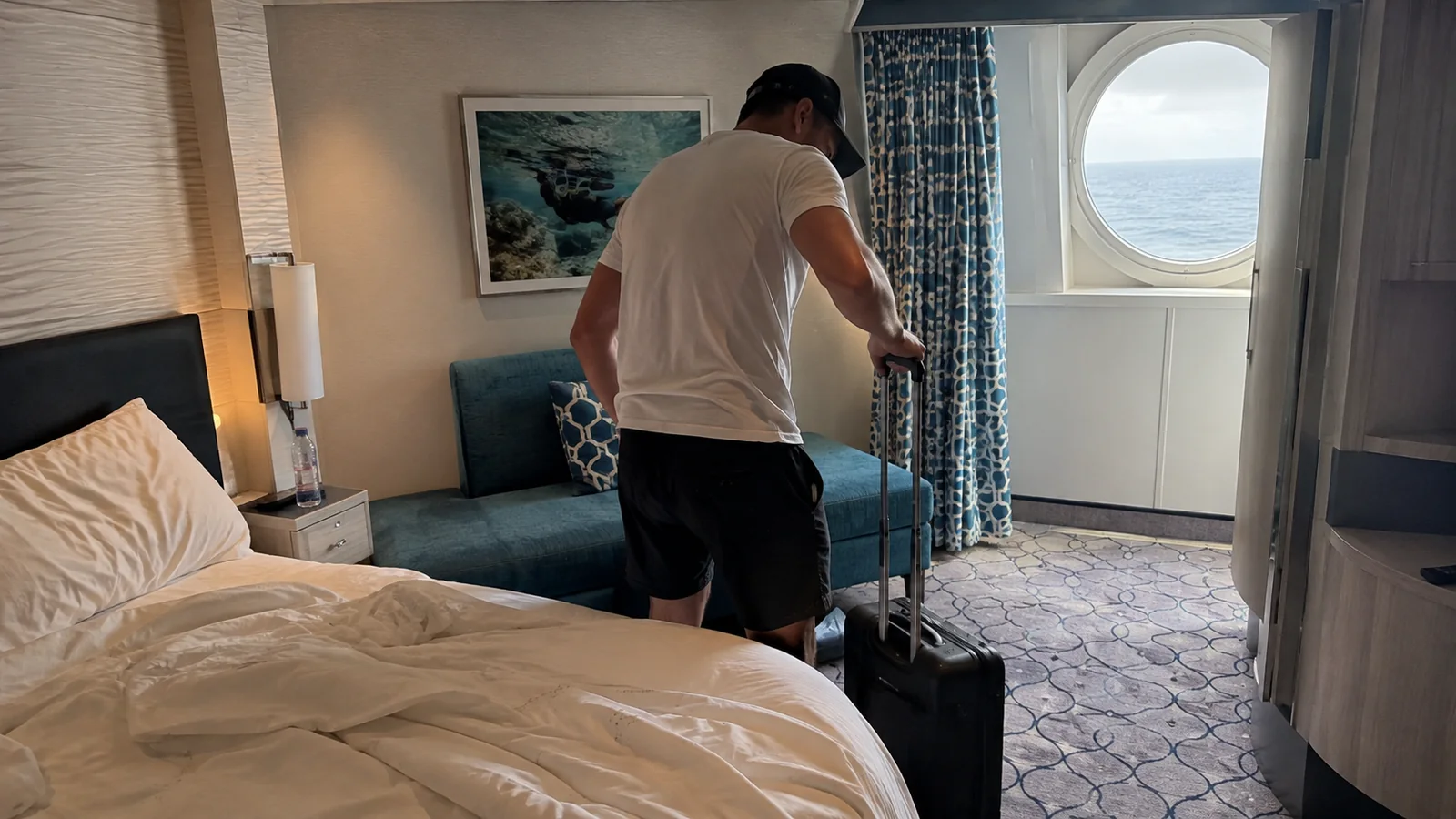 Passenger rolling a suitcase into a cabin with a round window.