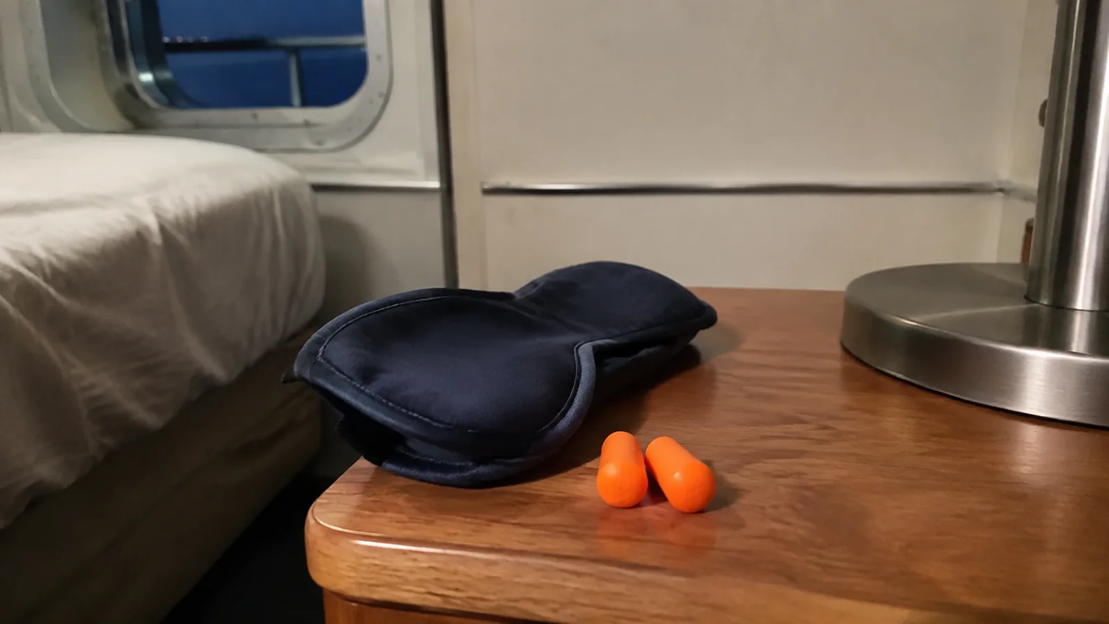 Sleep mask and earplugs beside a lamp on a cabin bedside table.
