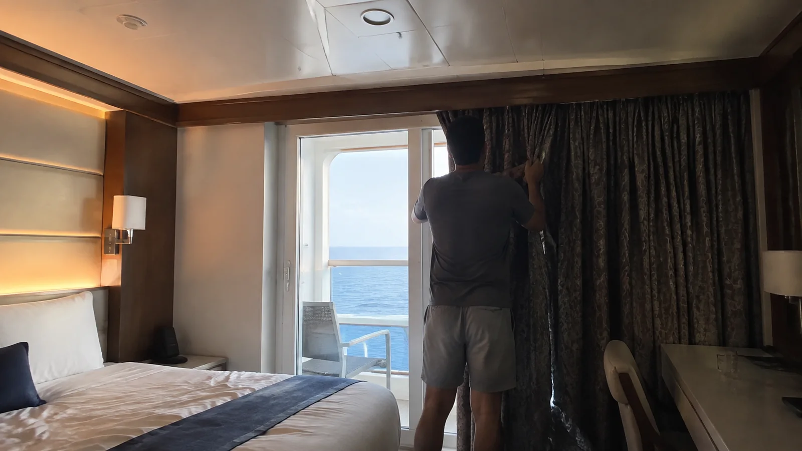 Passenger drawing curtains across the balcony doors of a cabin.