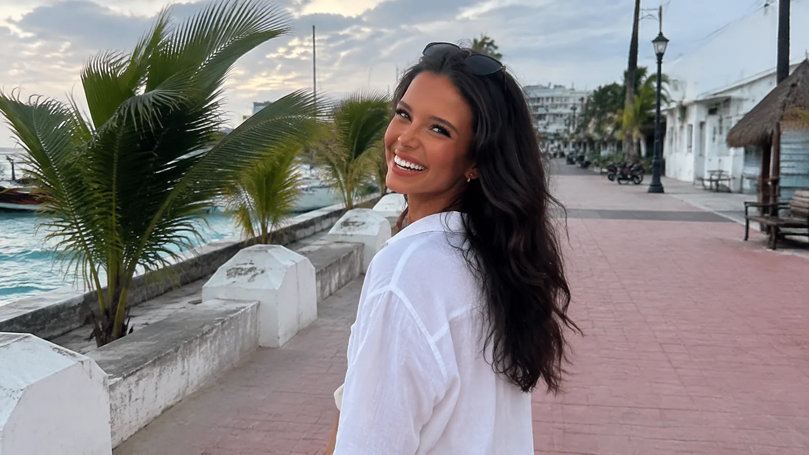 Smiling woman walking along a palm-lined seaside promenade