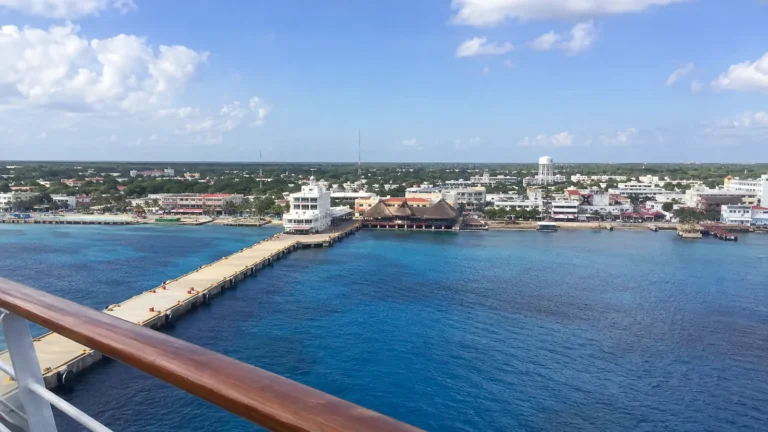 Long cruise pier leading toward a low coastal town across blue water.