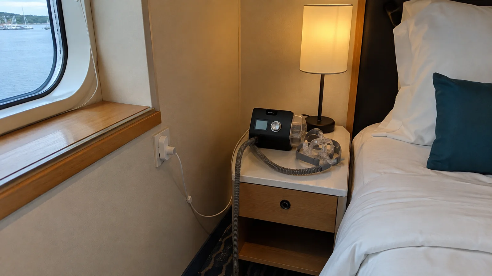 CPAP machine plugged in on a bedside table beneath a lamp.