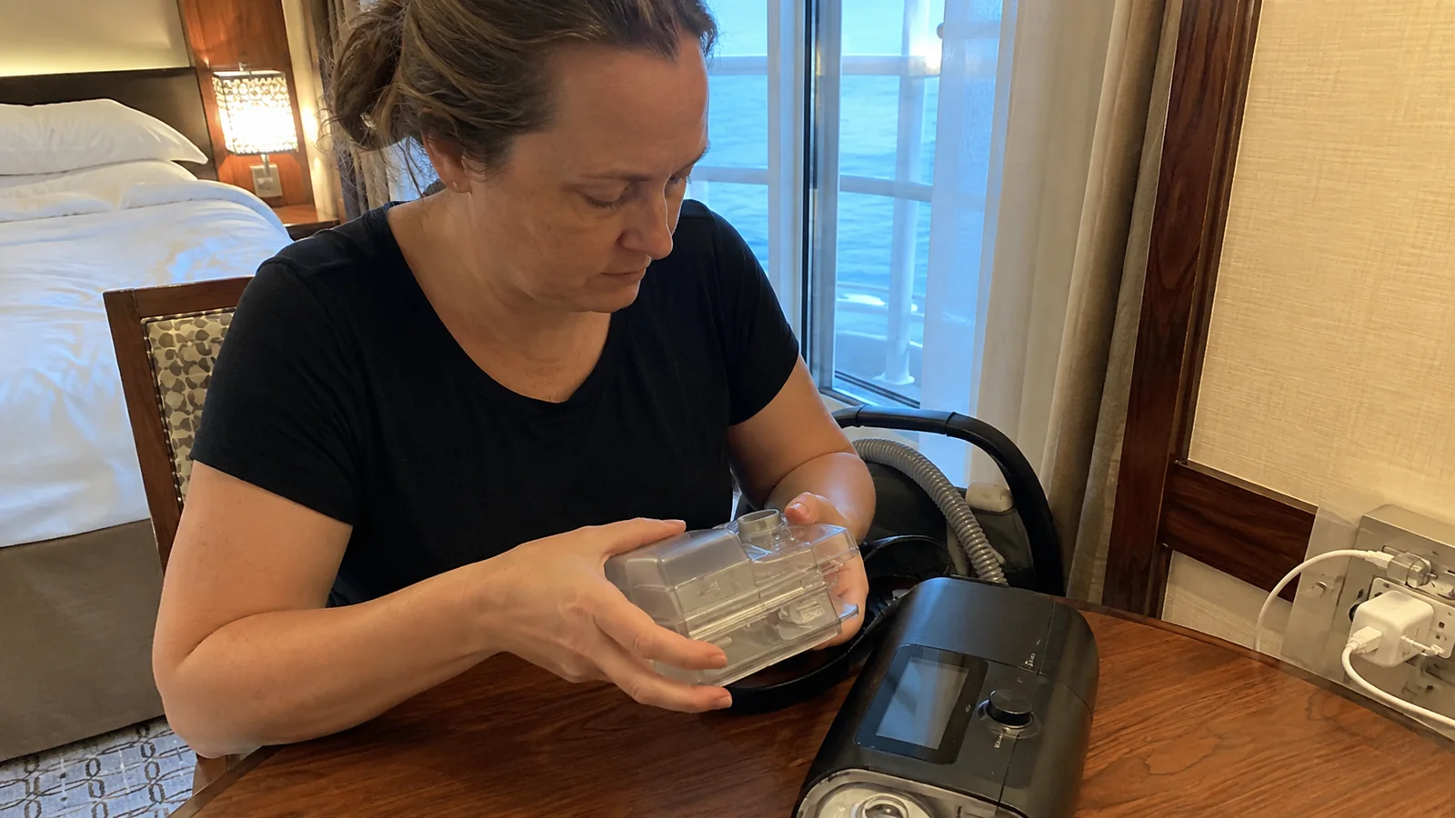 Woman checking a clear water chamber beside a CPAP travel bag.